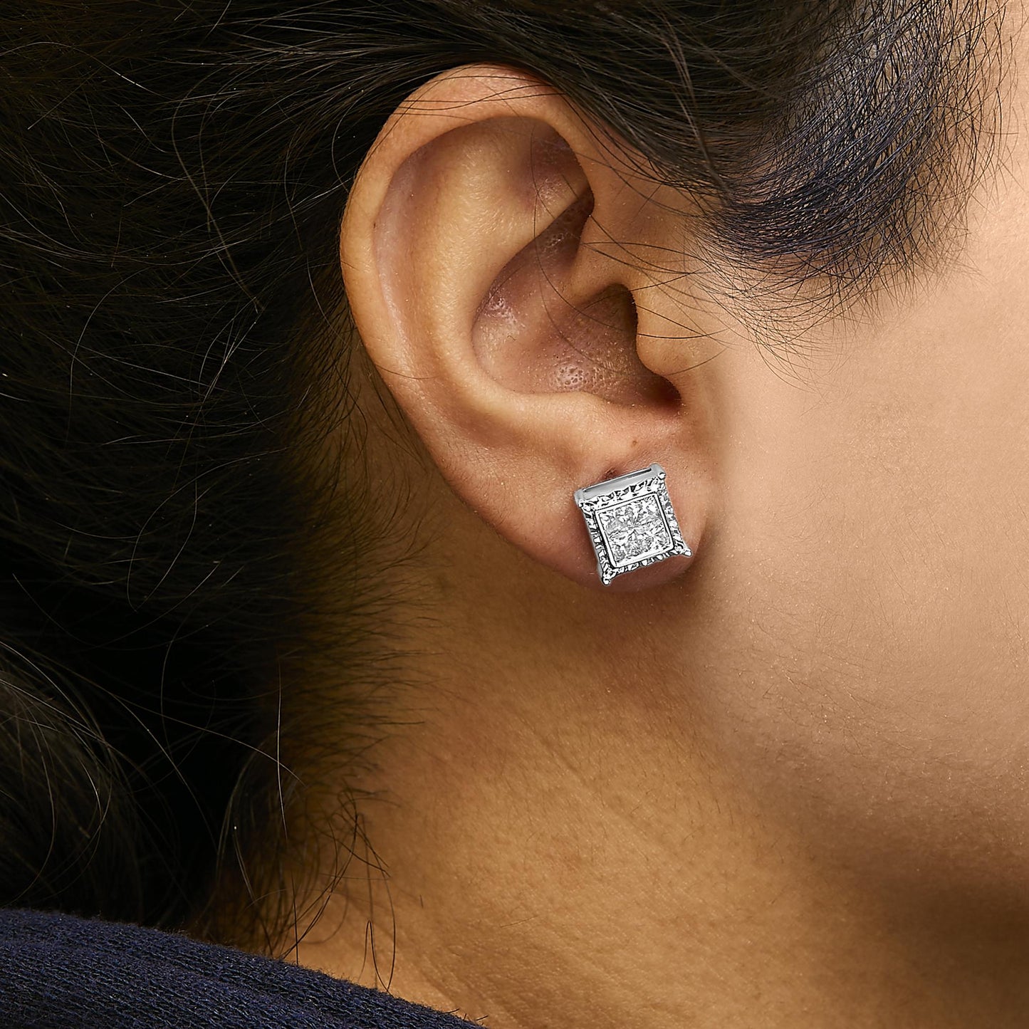 Close-up profile of a woman wearing white metal earrings with princess shape white gemstones in an invisible setting.