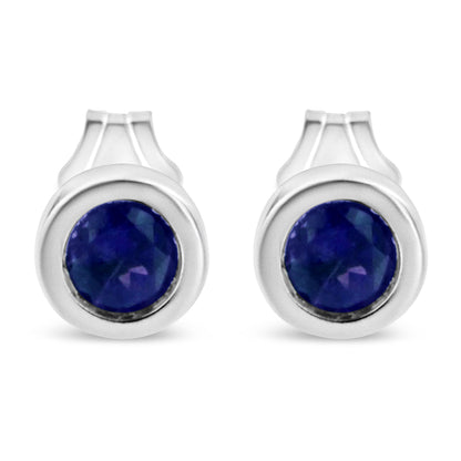 Front view of a pair of white metal stud earrings each featuring a round blue gemstone in a bezel setting.