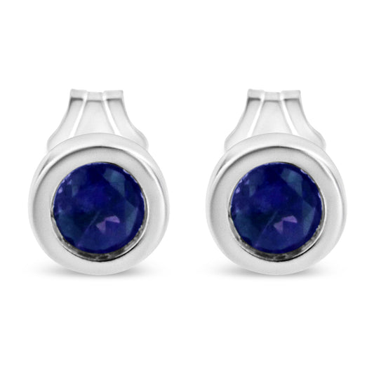 Front view of a pair of white metal stud earrings each featuring a round blue gemstone in a bezel setting.