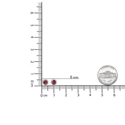 Pair of white metal stud earrings with round red gemstones in bezel setting, shown on a ruler and next to a coin for size reference, top-down view.