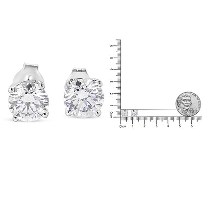 Front angle view of a pair of white metal stud earrings with round white gemstones in 4-prong settings, shown next to a ruler and coin for size reference.