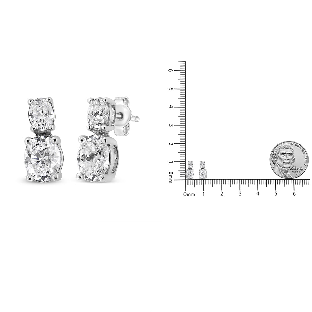 Pair of white metal earrings with two oval-shaped white gemstones in 4-prong settings, shown from a front and side angle, alongside a ruler and coin for size reference.