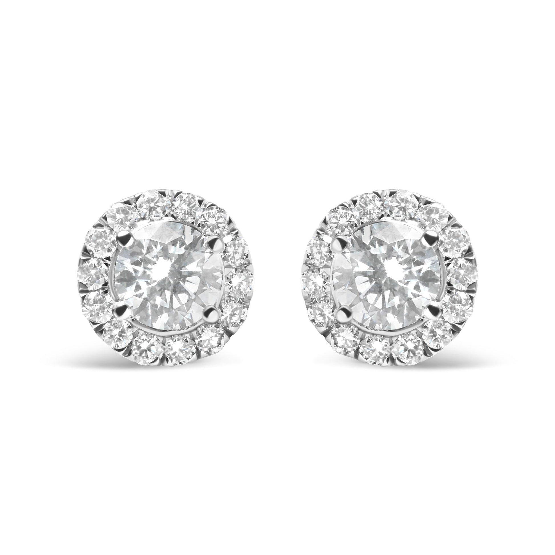Front view of a pair of white metal stud earrings each featuring a large round white gemstone surrounded by a halo of smaller round white gemstones in prong settings.