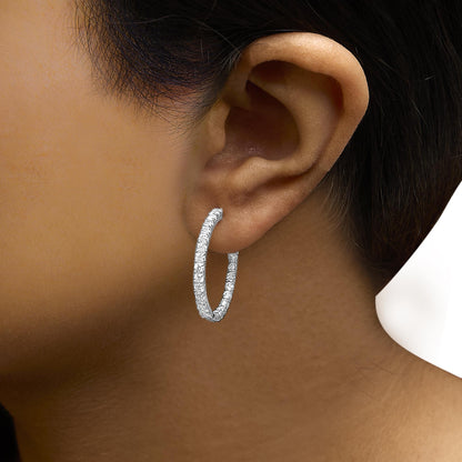 Close-up side view of a white metal hoop earring encrusted with round white gemstones, worn on a model's ear.