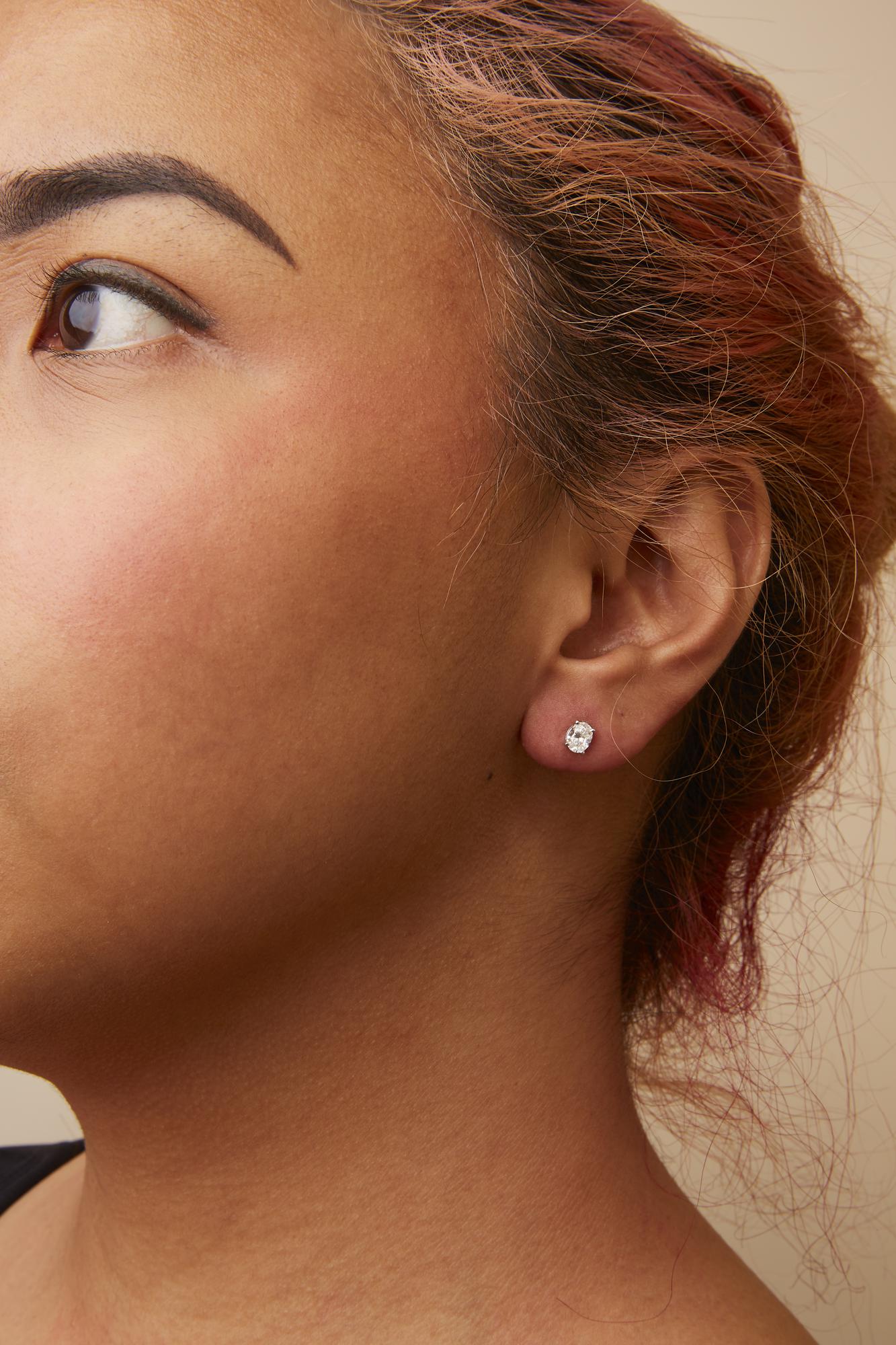 Close-up side view of a model wearing white metal stud earrings with oval-shaped white gemstones in a four-prong setting.