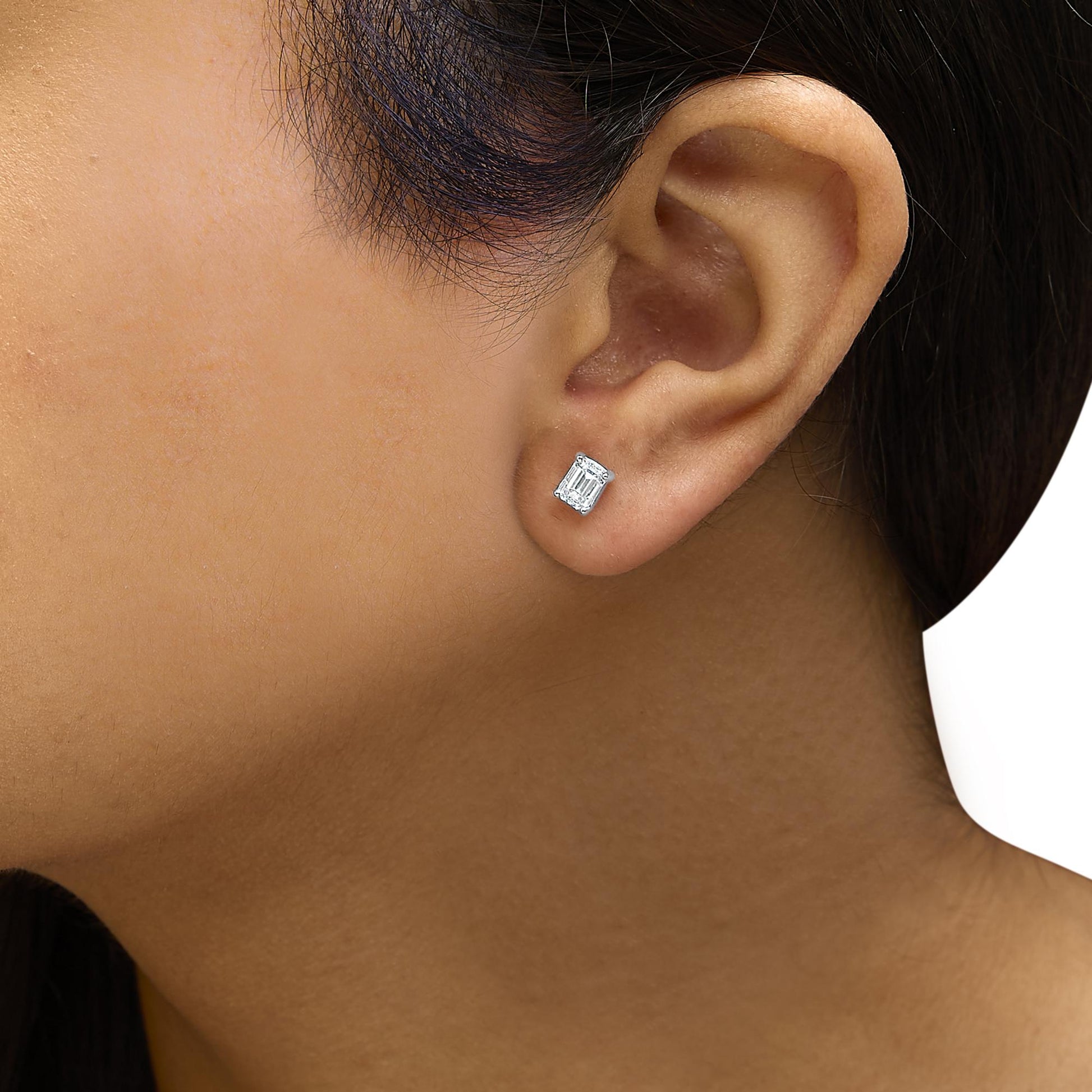 Close-up side view of a white metal stud earring with a rectangular emerald-shaped white gemstone, worn on a model's ear.