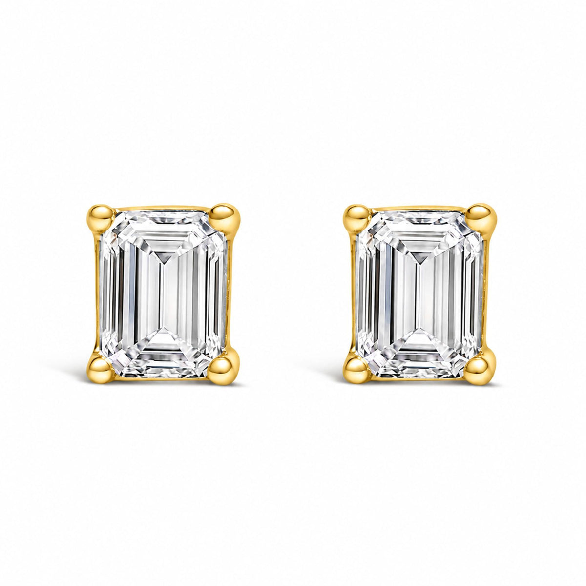 Close-up front view of a pair of yellow metal earrings with emerald-shaped white gemstones in a four-prong setting.