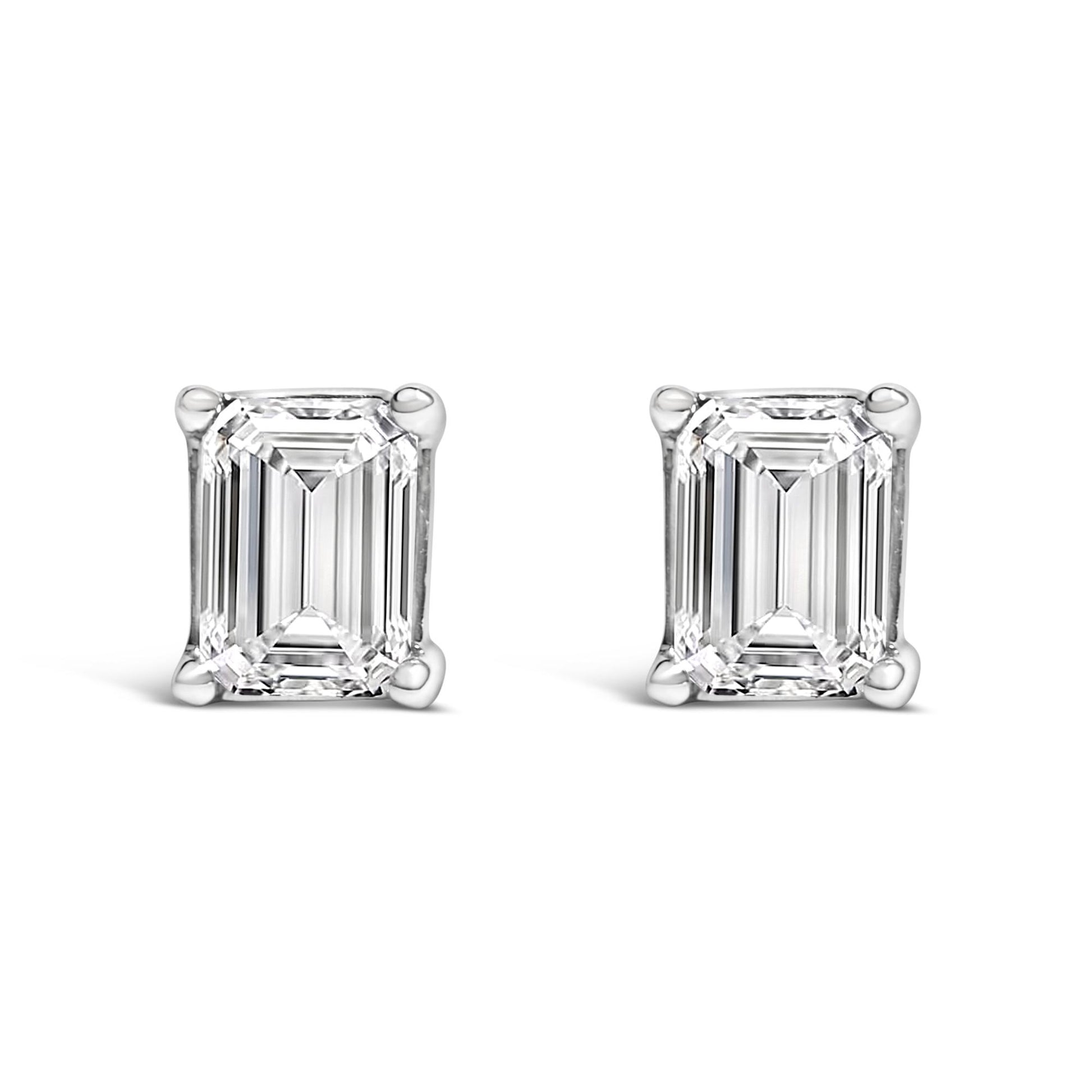 Front angle view of white metal stud earrings each featuring a single emerald-shaped white gemstone in a four-prong setting.