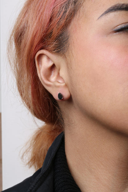 Close-up side view of a model wearing a white metal stud earring with a pear-shaped black gemstone in prong setting.