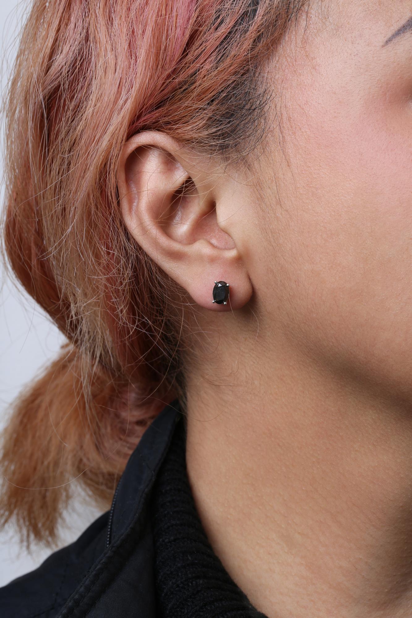 Close-up side view of a white metal stud earring with an oval-shaped black gemstone in prong setting, worn on a model's ear.