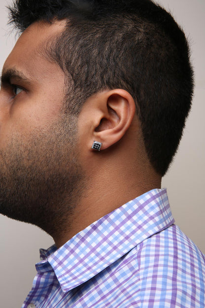 Side profile of a model wearing square yellow metal earrings with black and white round gemstones in prong settings.