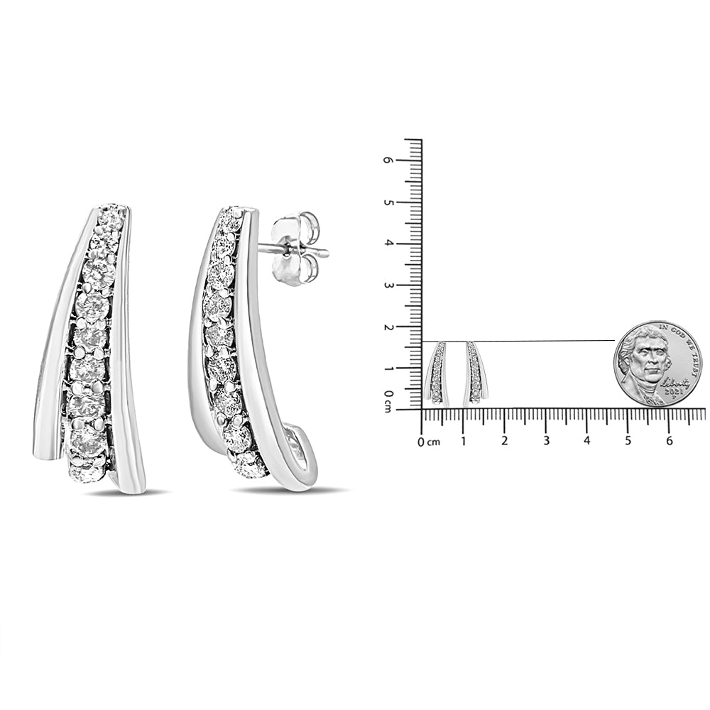 Close-up front and side view of white metal earrings with a curved design and a row of round white gemstones in prong settings, shown next to a ruler and a coin for size reference.