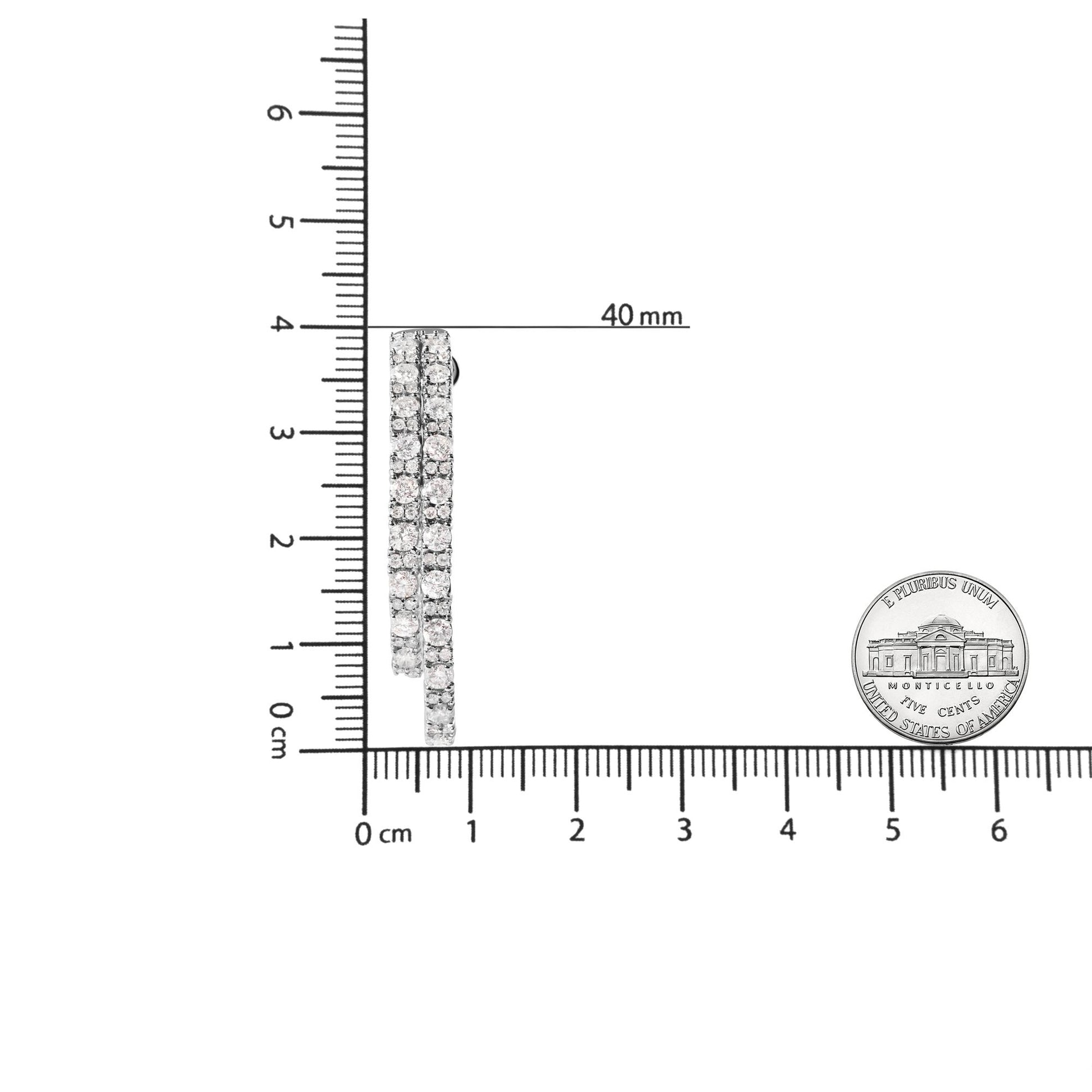 Side view of white metal earrings with three rows of round white gemstones in prong settings, shown on a ruler and next to a coin for size reference.