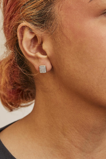 Close-up side view of a model wearing square yellow metal earrings encrusted with small round white gemstones in a prong setting.