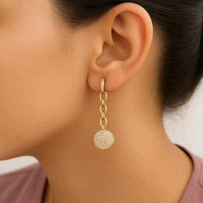 Close-up side view of a model wearing a yellow metal dangle earring with three linked oval shapes and a circular pendant encrusted with white round prong-set gemstones.