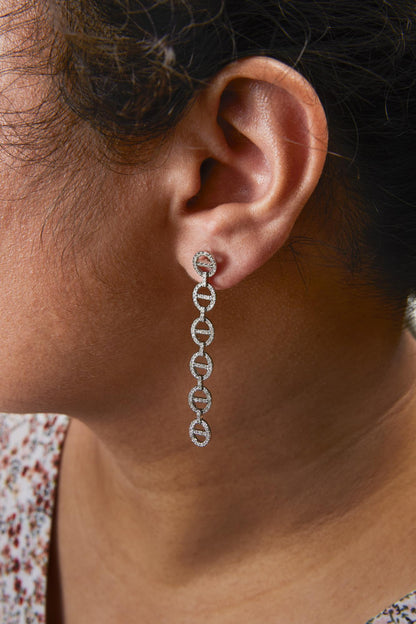 Close-up side view of a model wearing long white metal earrings featuring linked circular shapes encrusted with small round white gemstones in prong settings.