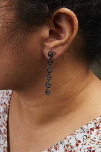 Close-up side view of a model wearing long white metal earrings composed of linked circular shapes, each adorned with small round blue gemstones in a prong setting.