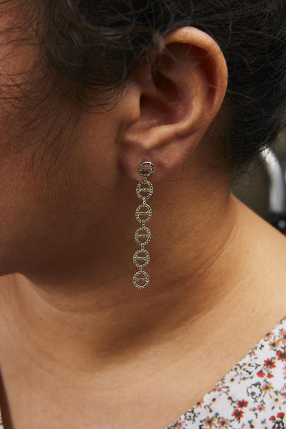 Close-up side view of a model wearing a long white metal earring composed of linked circular shapes, each adorned with small yellow round gemstones in prong settings.