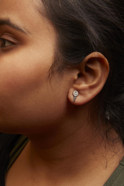 Close-up side view of a model wearing white metal earrings with a circular top encrusted with white gemstones and a small key-shaped dangle.