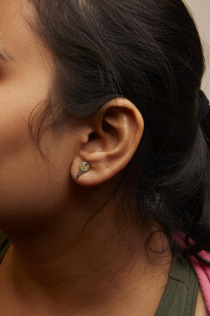 Close-up side view of a model wearing a white metal earring shaped like a key with round yellow gemstones in a prong setting on the round top part.