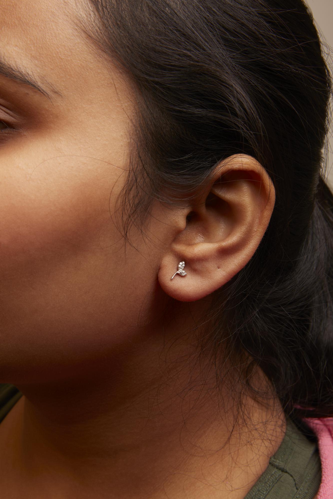 Close-up side view of a model wearing white metal earrings shaped like a small branch with round white gemstones in prong settings.