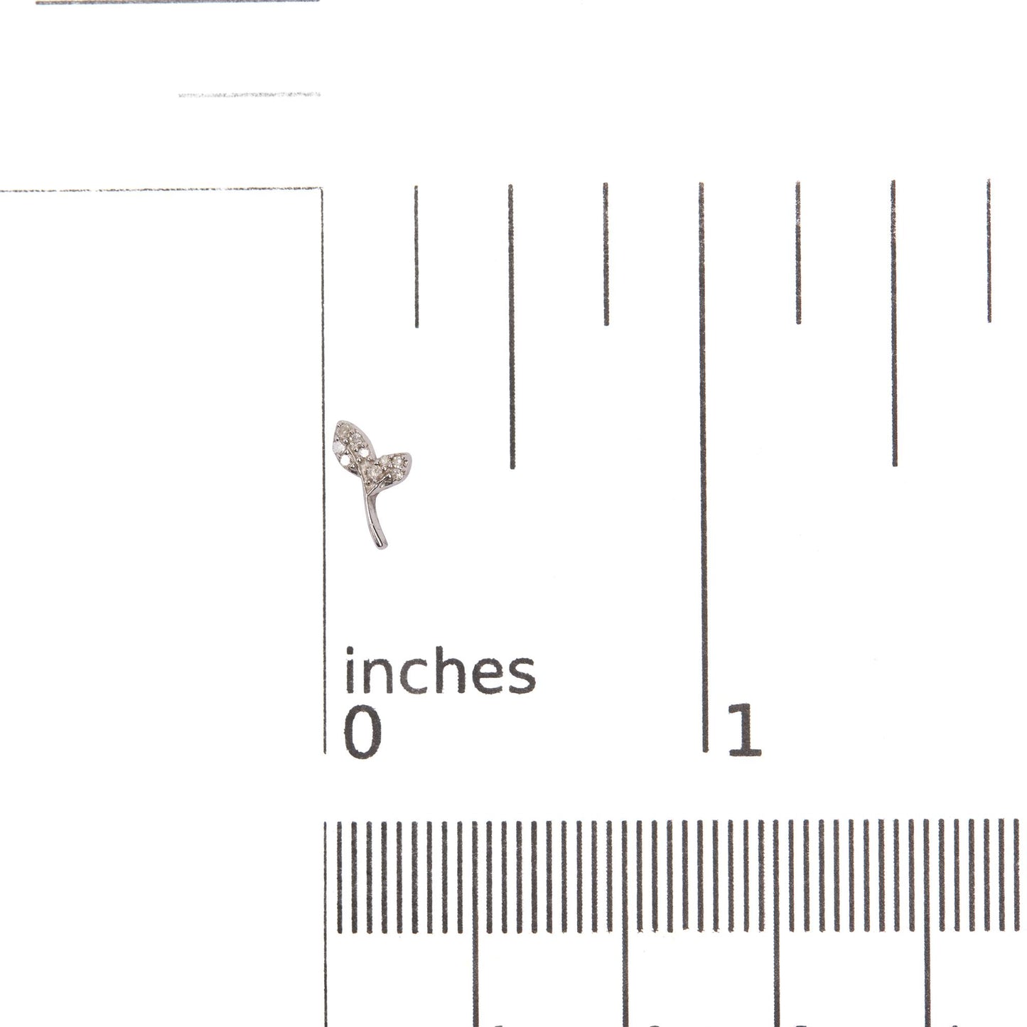 Close-up front angle of a white metal earring in the shape of a small branch with two leaves, each leaf set with multiple small round white gemstones, shown on a ruler scale for size reference.