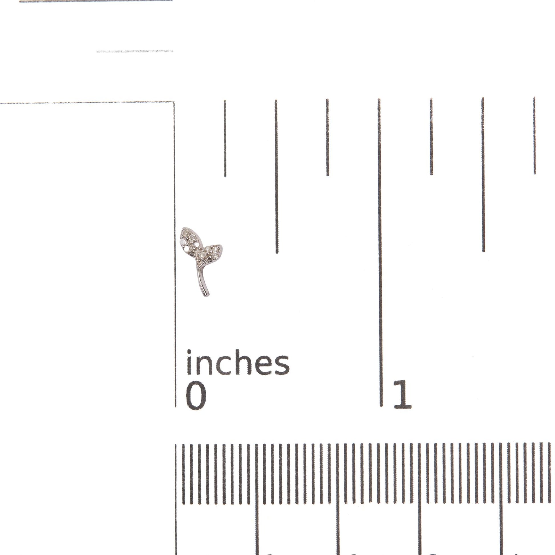Close-up front angle of a white metal earring in the shape of a small branch with two leaves, each leaf set with multiple small round white gemstones, shown on a ruler scale for size reference.