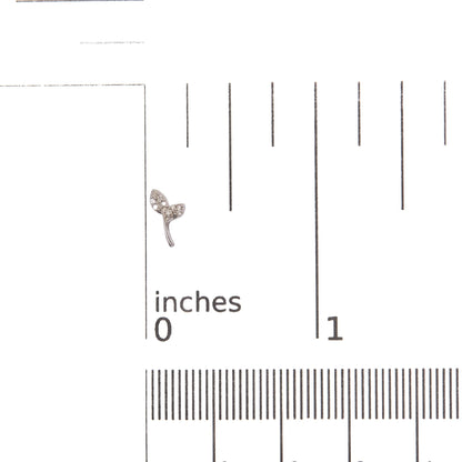 Close-up front angle of a white metal earring in the shape of a small branch with two leaves, each leaf set with multiple small round white gemstones, shown on a ruler scale for size reference.