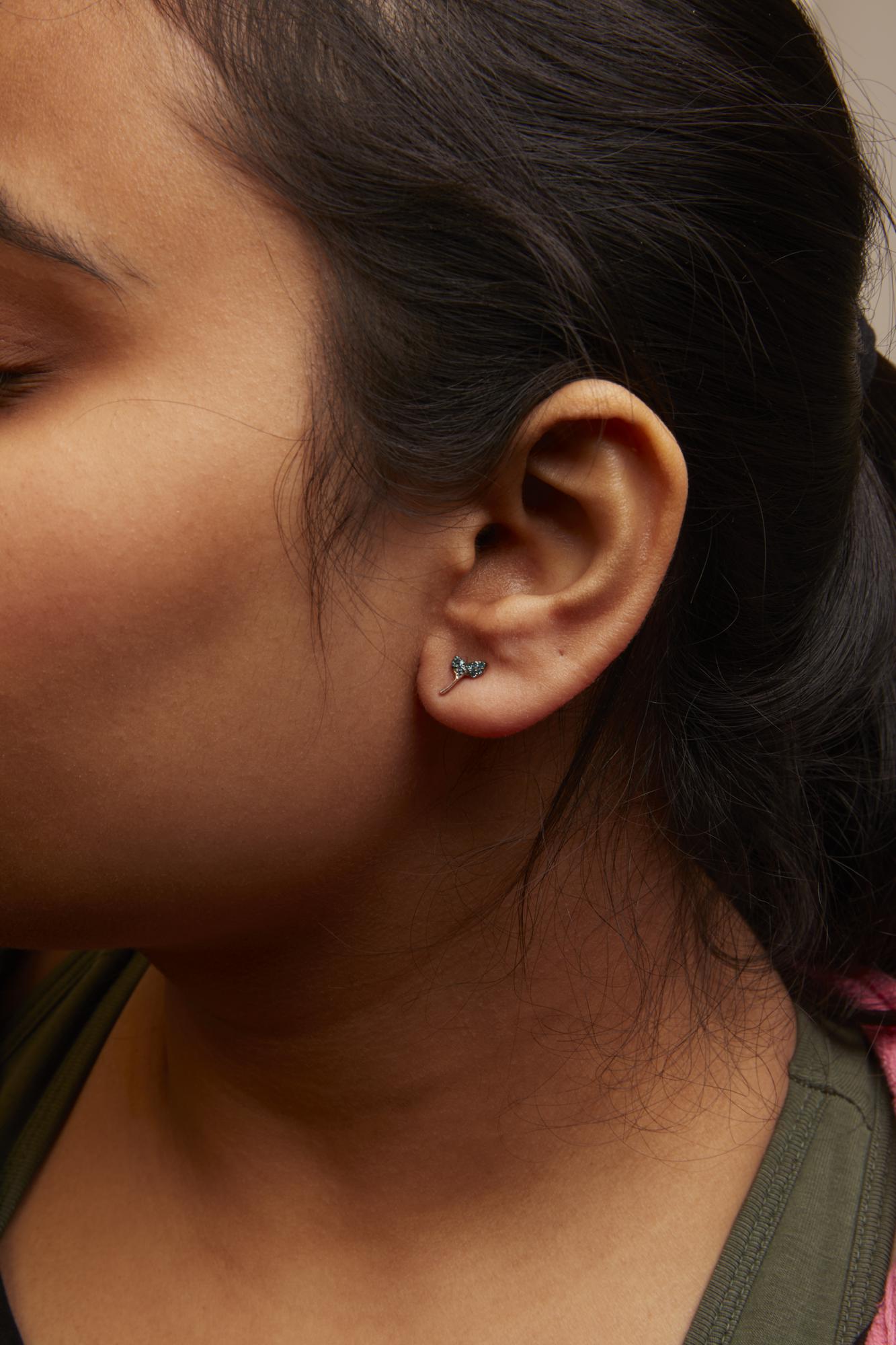 Close-up side view of a model wearing white earrings shaped like a small branch with round blue gemstones in a prong setting.