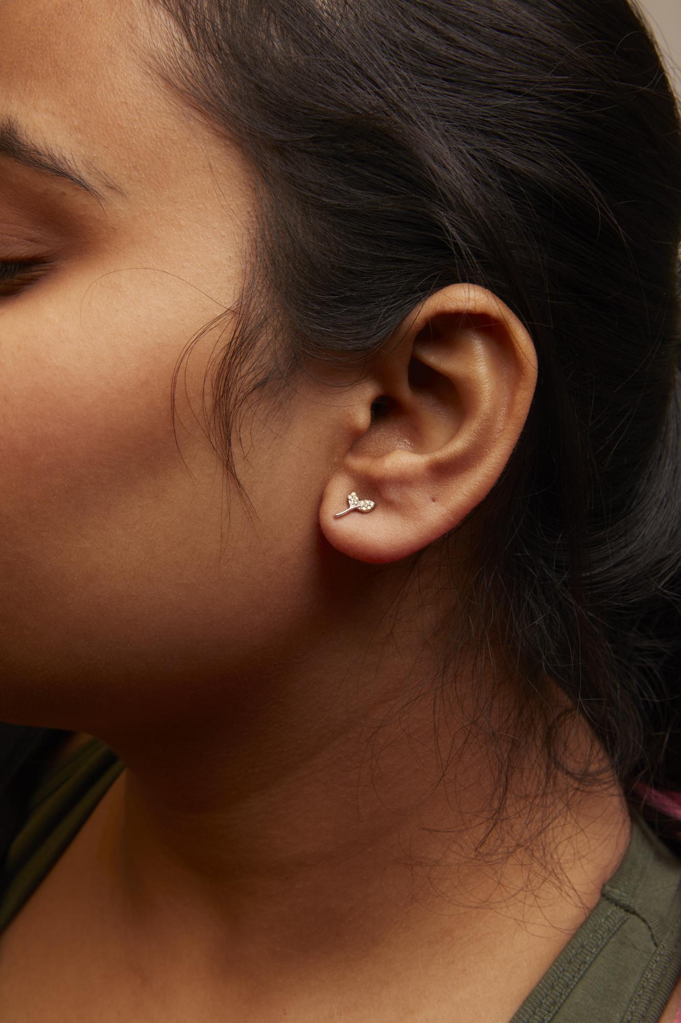 Close-up side view of a model wearing a pair of white metal earrings with multiple small round yellow gemstones set in prong settings.