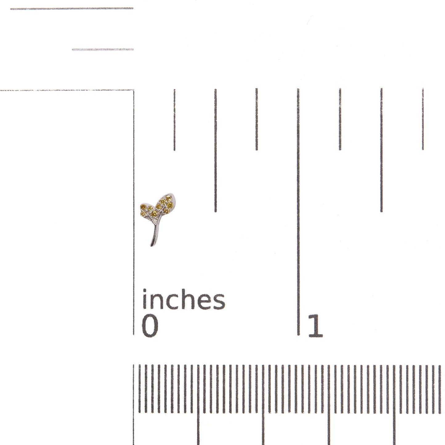Close-up front angle of a white metal earring shaped like a small branch with three leaves, each leaf adorned with round yellow gemstones in prong settings, shown on a ruler for scale.