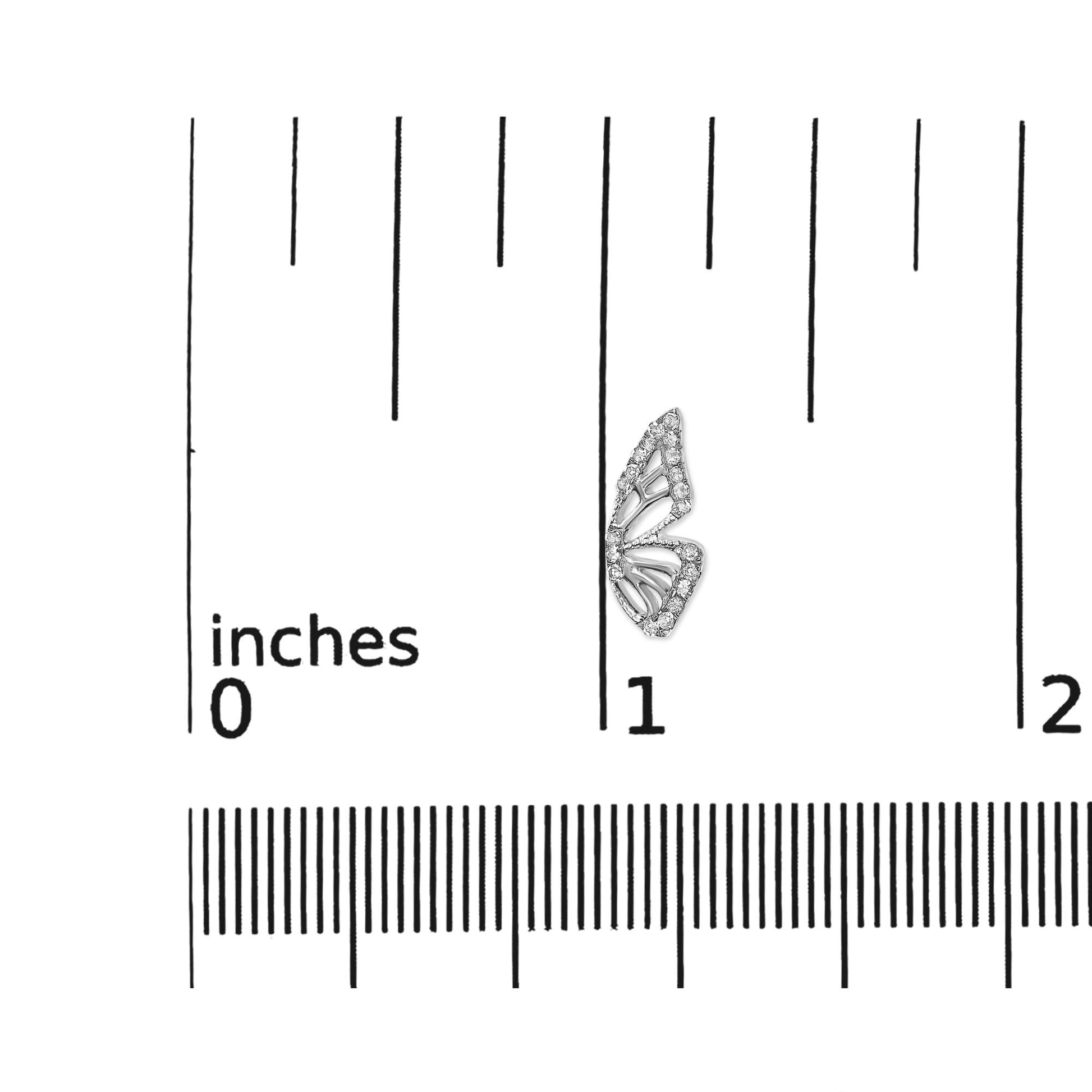 Close-up front angle of a single white earring shaped like a stylized butterfly wing, outlined with round white gemstones in prong settings, shown on a ruler scale.