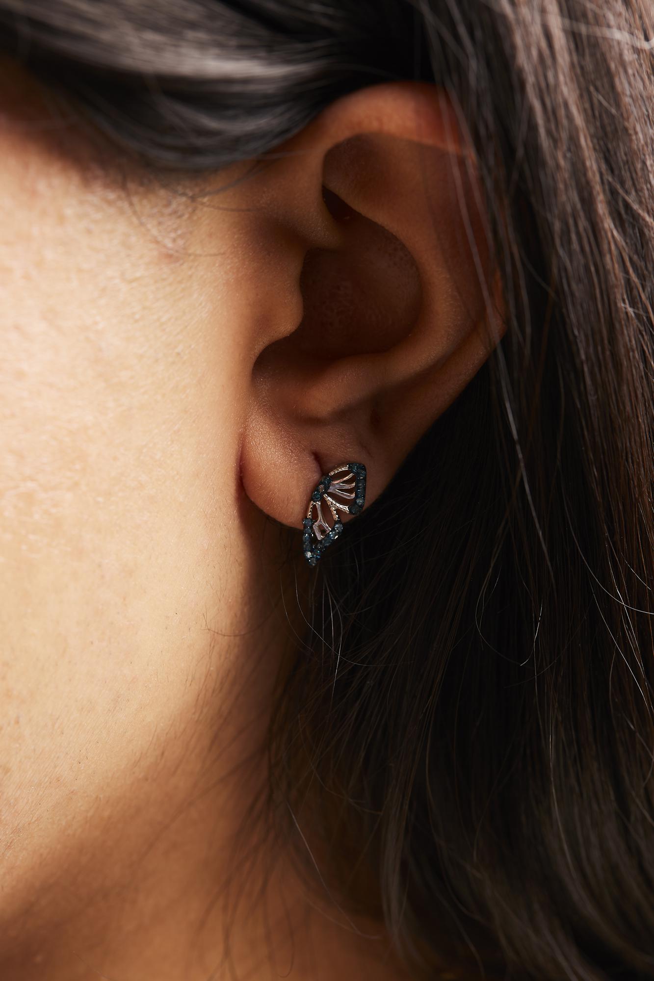Close-up side view of a model wearing white metal earrings with an abstract fan shape, adorned with round blue gemstones in prong settings.