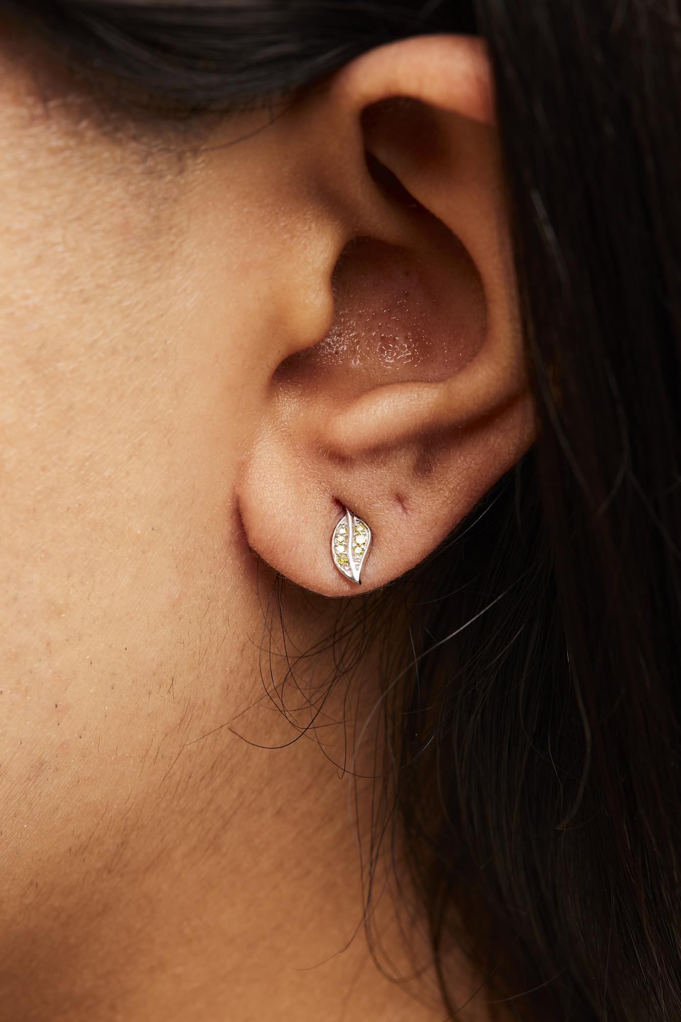 Close-up side view of a white metal earring with small round prong-set yellow gemstones, worn on a model's ear.