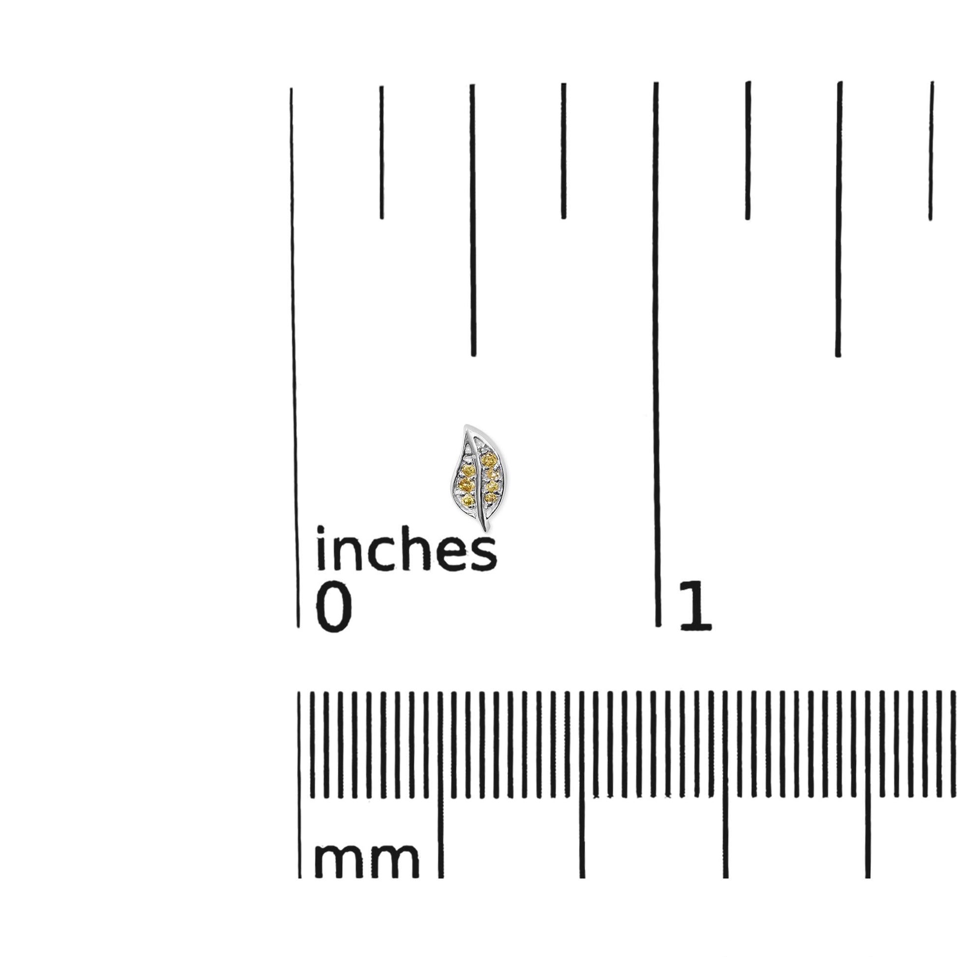 Close-up front view of a white metal leaf-shaped earring with multiple small round yellow gemstones in prong settings, placed on a ruler for size reference.
