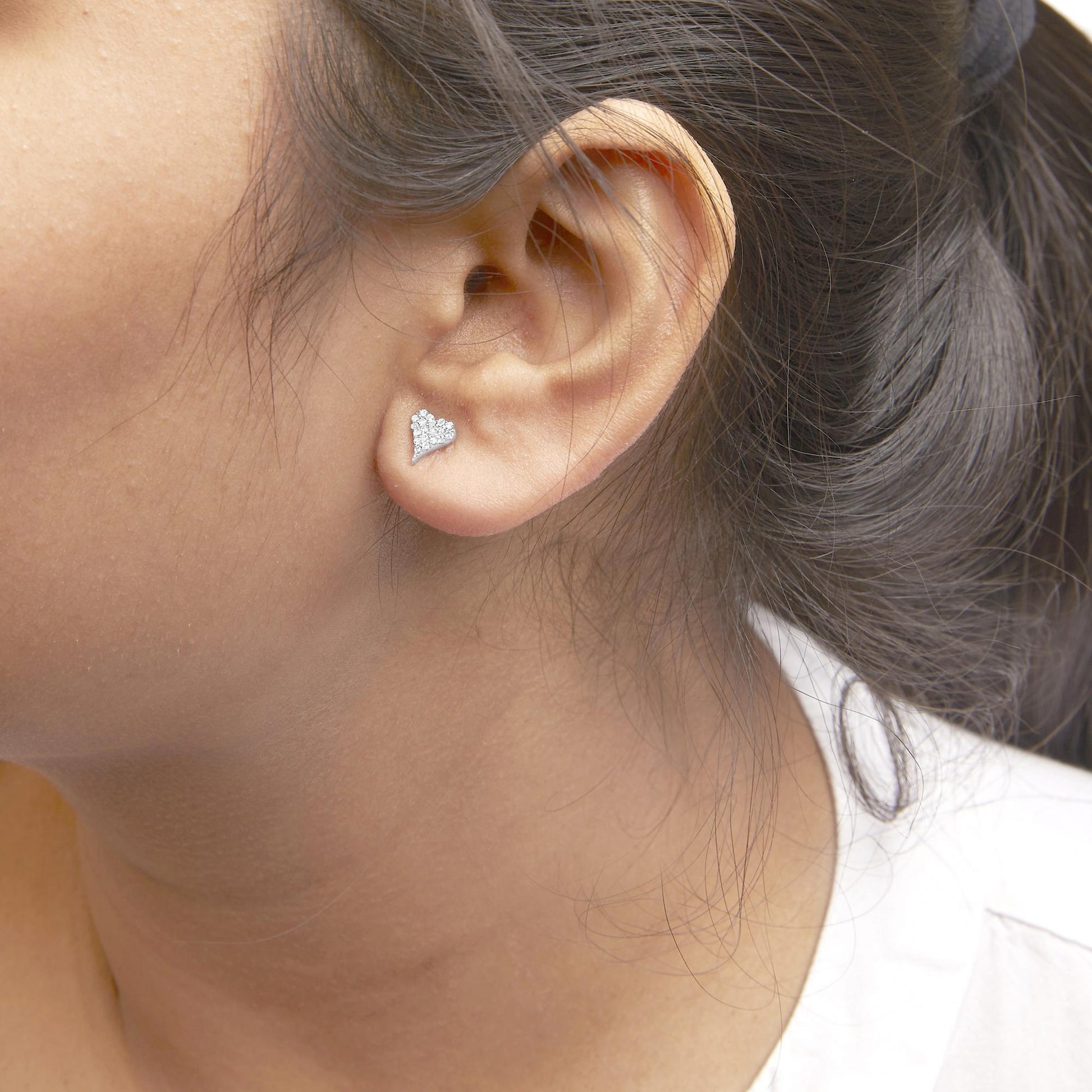 Close-up side view of a model wearing a white metal heart-shaped earring with multiple round white gemstones in prong settings.
