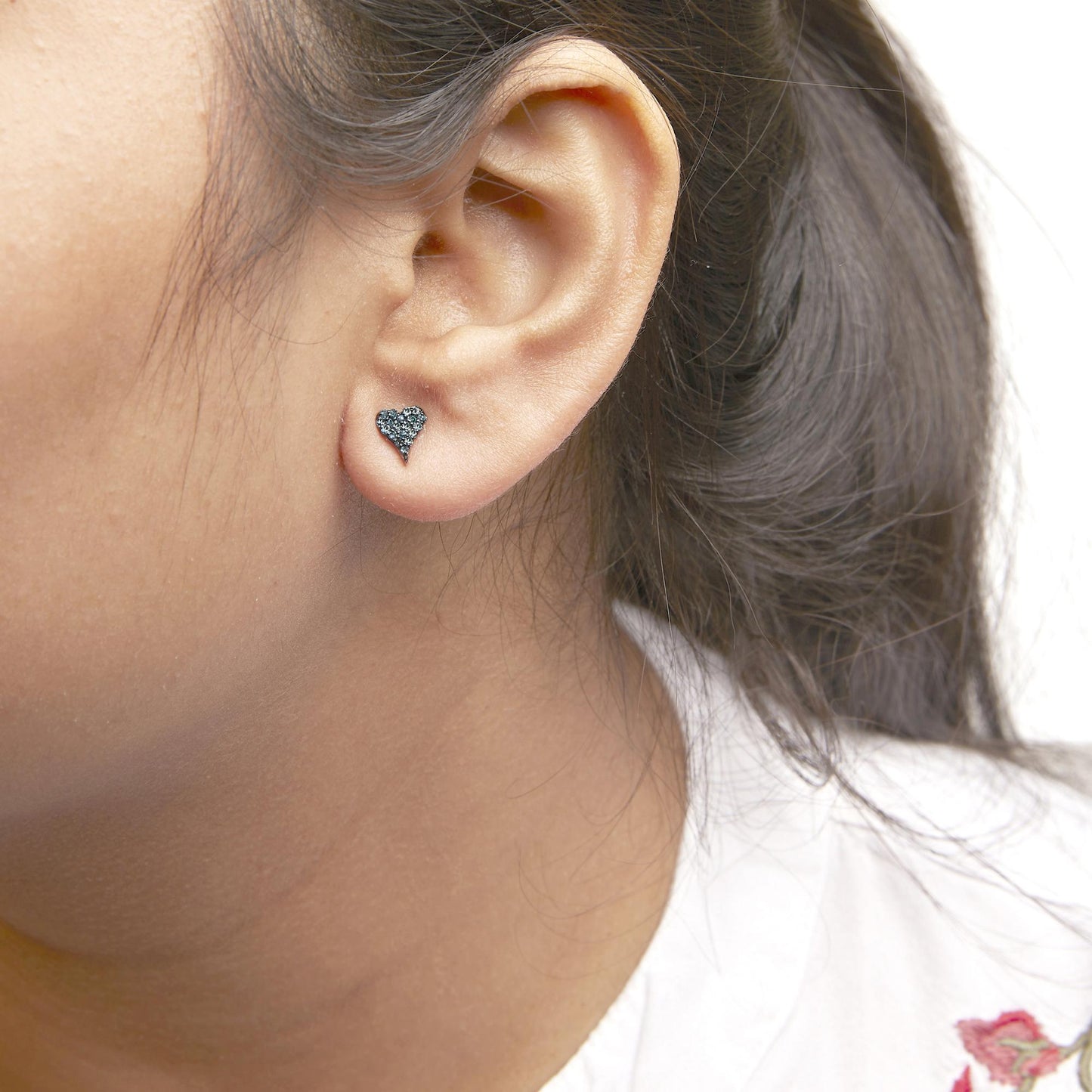 Close-up side view of a white metal heart-shaped stud earring with multiple round blue gemstones worn on a model's ear.