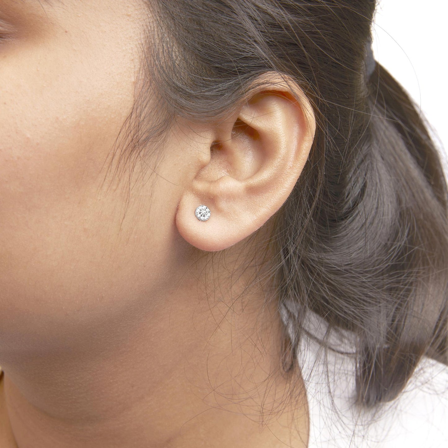 Close-up side view of a model wearing a pair of white metal stud earrings with round white gemstones in prong settings.
