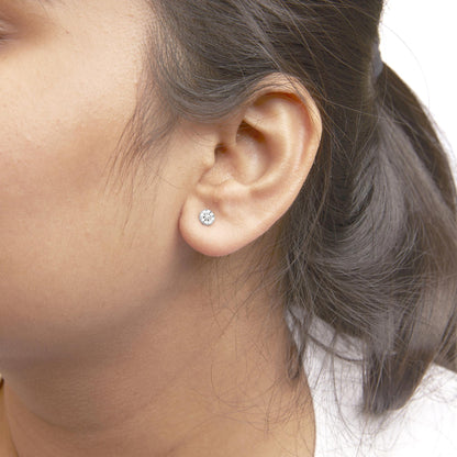 Close-up side view of a model wearing a pair of white metal stud earrings with round white gemstones in prong settings.