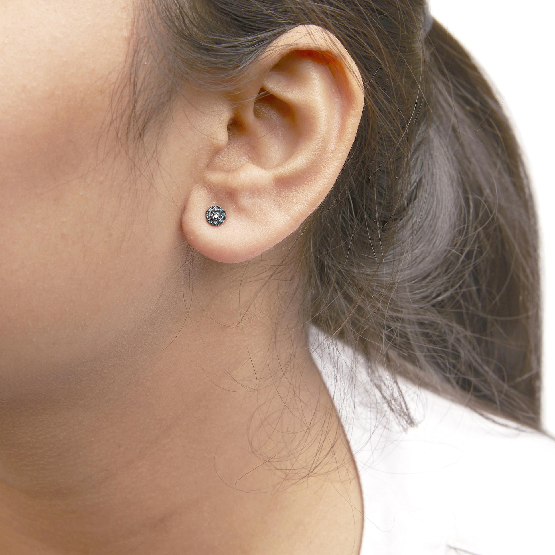 Close-up side view of a white metal stud earring with round blue gemstones in prong setting, worn on a model's ear.