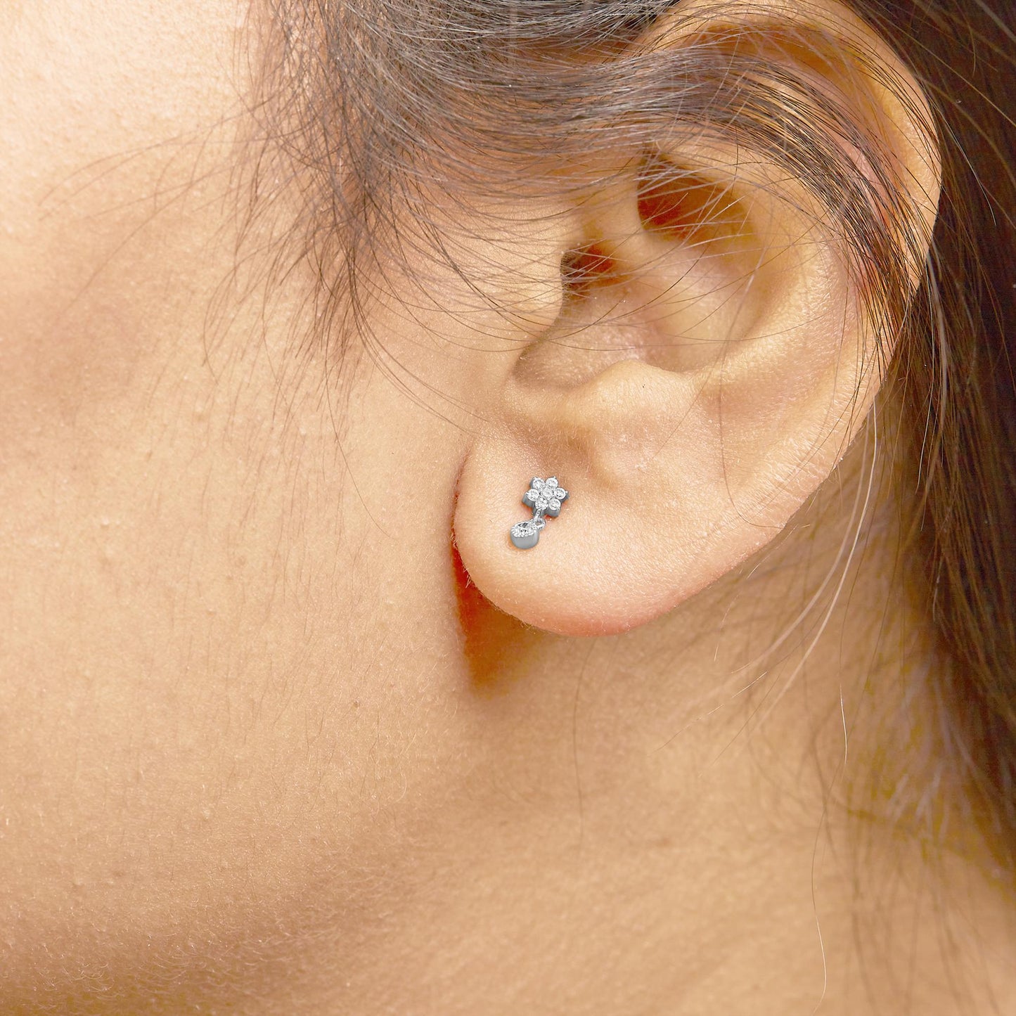 Close-up side view of white metal earrings with round white gemstones in prong settings, worn on a model's ear.