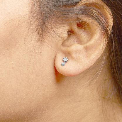 Close-up side view of white metal earrings with round white gemstones in prong settings, worn on a model's ear.
