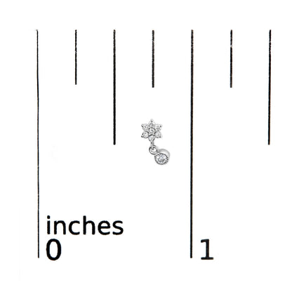 Close-up of white metal earring with small round prong-set white gemstones arranged in a flower shape and a single gemstone dangle, placed on a ruler for size reference.