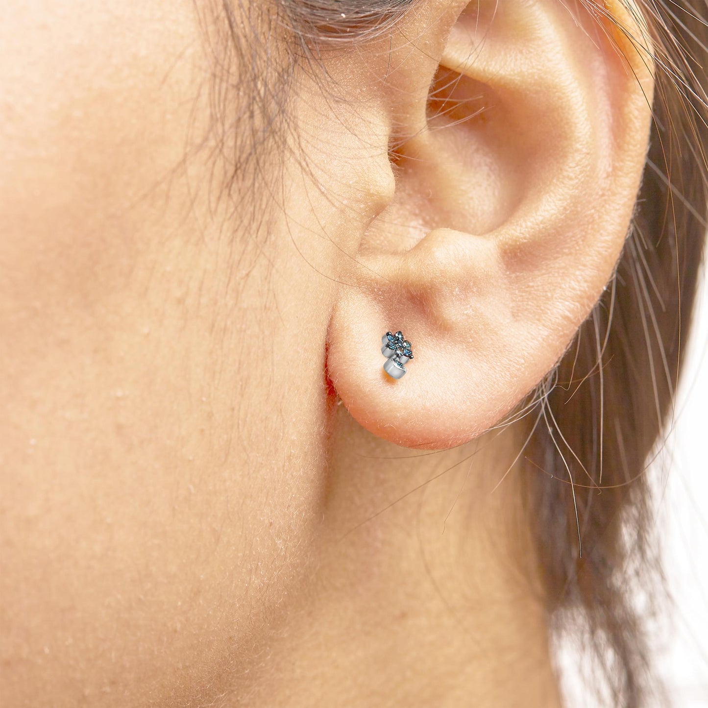Close-up side view of a model wearing white metal stud earrings featuring round blue gemstones in a prong setting.