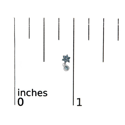 White metal earrings with blue round prong-set gemstones, shaped like a small flower with a dangling gemstone, shown on a ruler for size reference, top-down angle.