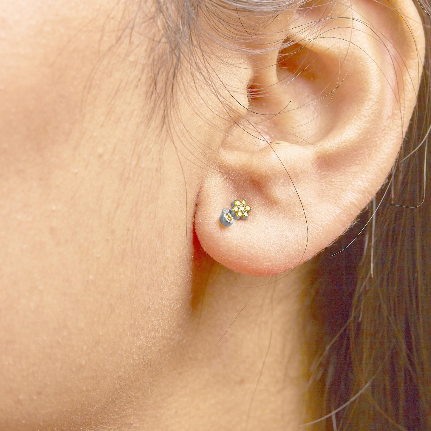 Close-up side angle of a white metal stud earring with multiple small round yellow gemstones in a cluster, worn on a model's ear.