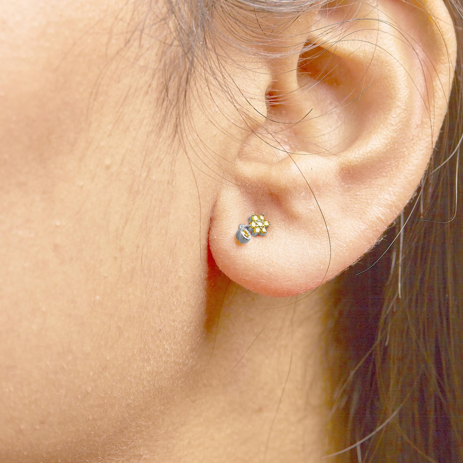 Close-up side angle of a white metal stud earring with multiple small round yellow gemstones in a cluster, worn on a model's ear.