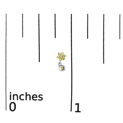 Close-up front view of white metal earrings with cluster of yellow round gemstones in prong setting and a single dangling yellow round gemstone, placed on a ruler for size reference.