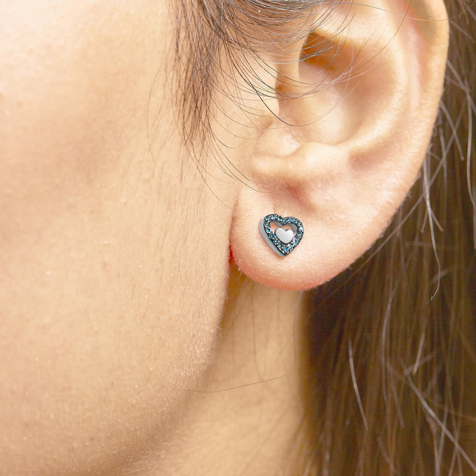 Close-up side view of a white heart-shaped earring with blue round gemstones in prong setting, worn on a model's ear.