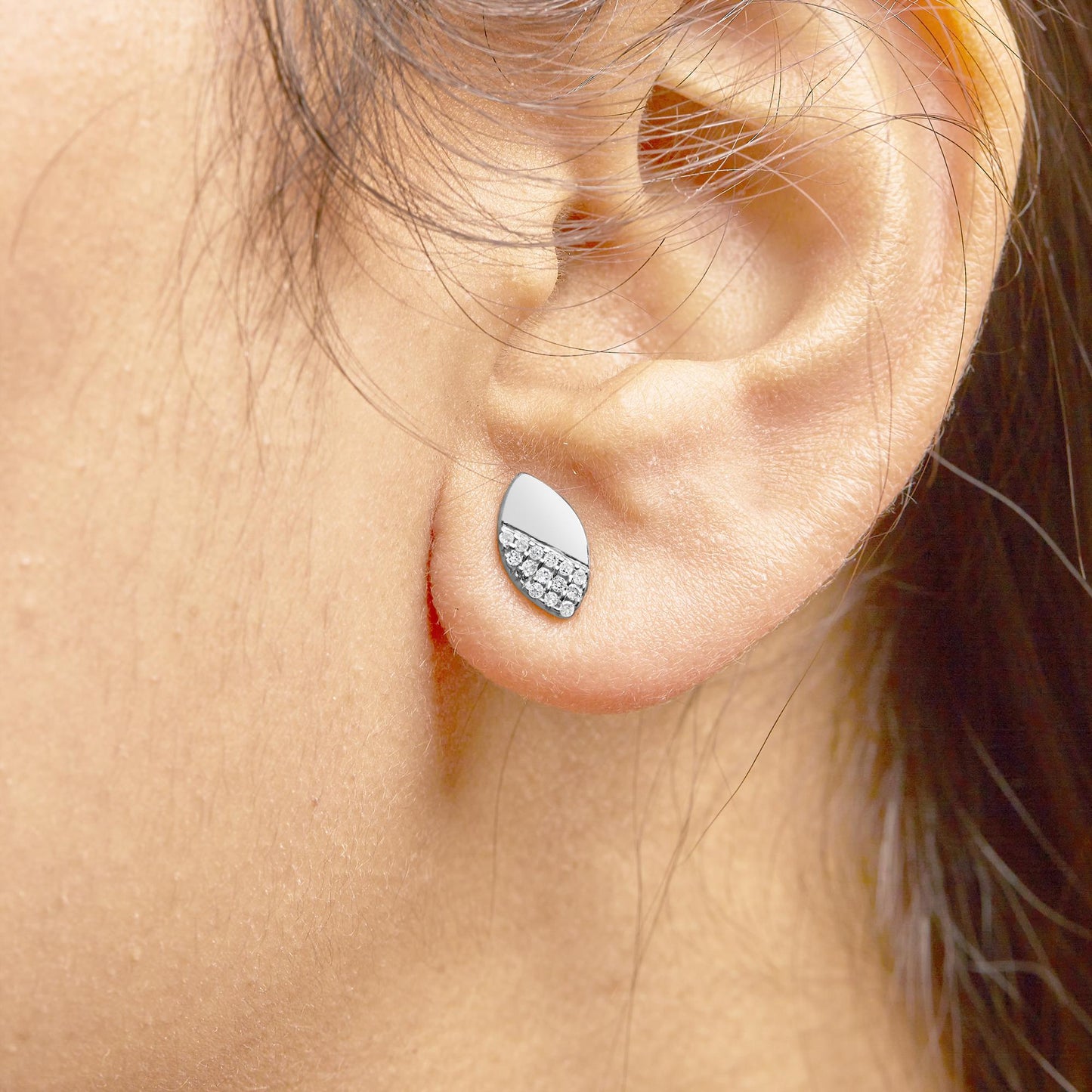 Close-up side view of a white metal teardrop-shaped earring with round white gemstones in a prong setting worn on a model's ear.
